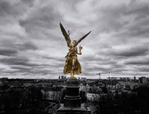 Der Friedensengel in Gold vor Münchens Stadtbild in schwarz-weiß. Fotografie von James Murray.